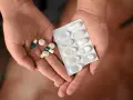 Dłonie trzymające tabletki i blister. Wśród nich są leki, które mogą być inhibitorami pompy protonowej, pomagając w leczeniu dolegliwości żołądkowych.