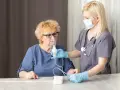 Pielęgniarka pomaga starszej kobiecie z inhalatorem. Pytanie brzmi, ile dni można robić inhalacje z soli fizjologicznej.