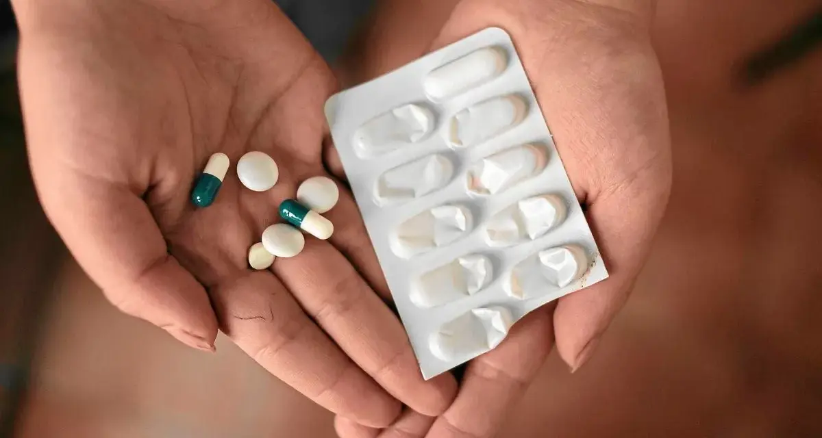 Dłonie trzymające tabletki i blister. Wśród nich są leki, które mogą być inhibitorami pompy protonowej, pomagając w leczeniu dolegliwości żołądkowych.