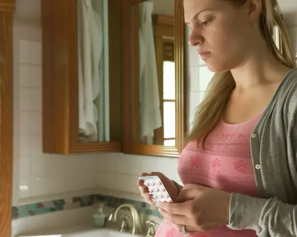 Zmartwiona ciężarna kobieta trzyma blister tabletek. Czy amoksycylina w ciąży jest bezpieczna?
