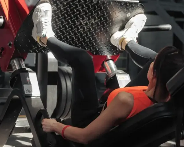 Kobieta ćwiczy na maszynie do wyciskania nóg, wykonując ćwiczenie push pull legs.
